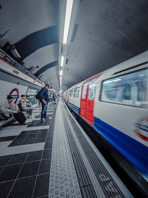 Interior view of Waterloo Station underground platform with grey tiled wall featuring a large circular London Underground roundel sign displaying 'Waterloo' in white on a blue background; the platform